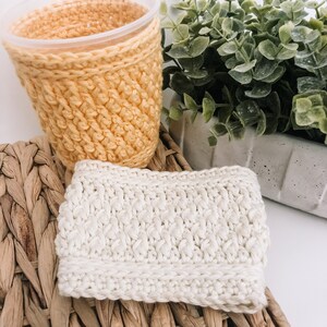 May include: Two crocheted cup cozies, one in a light yellow color and the other in a white color. The cozies are made with a textured stitch pattern.