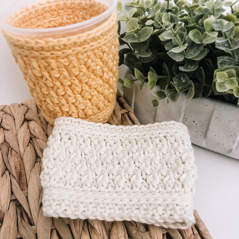 May include: Two crocheted cup cozies, one in a light yellow color and the other in a white color. The cozies are made with a textured stitch pattern.