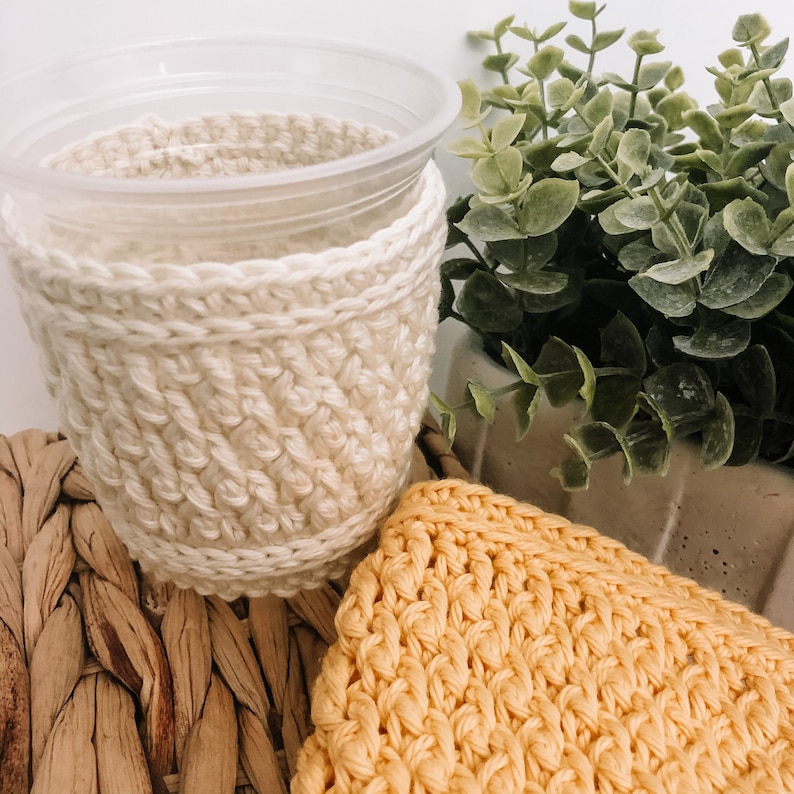 May include: A close-up of two crocheted cup cozies. One is a cream-colored cozy with a simple stitch pattern. The other is a yellow cozy with a more intricate stitch pattern. Both cozies are made with soft yarn and are perfect for keeping your hands warm while enjoying your favorite beverage.
