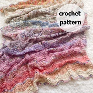 Op de afbeelding: Een veelkleurig gehaakt deken met een golvend patroon. Het deken is gemaakt met verschillende tinten roze, paars, blauw en crème.