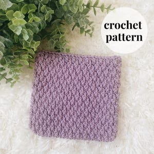 May include: A close-up of a purple crochet square with a textured stitch pattern. The square is on a white fluffy surface. crochet pattern