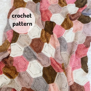 May include: A crochet blanket with a hexagonal pattern in shades of pink, brown, gray, and white. The blanket is made with a variety of stitches and textures, creating a unique and interesting design. The text "crochet pattern" is written on a pink circle in the upper left corner of the image.