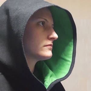 May include: A person wearing a black hooded sweatshirt with a green lining. The hood is pulled up over their head, and they are looking to the right.