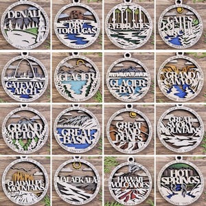 Puede incluir: Doce adornos de madera que representan diferentes parques nacionales de los Estados Unidos. Cada adorno es redondo y presenta una ilustraci&oacute;n detallada de un hito del parque, junto con el nombre del parque y sus coordenadas. Los adornos est&aacute;n pintados en varios tonos de marr&oacute;n, azul, verde y blanco.