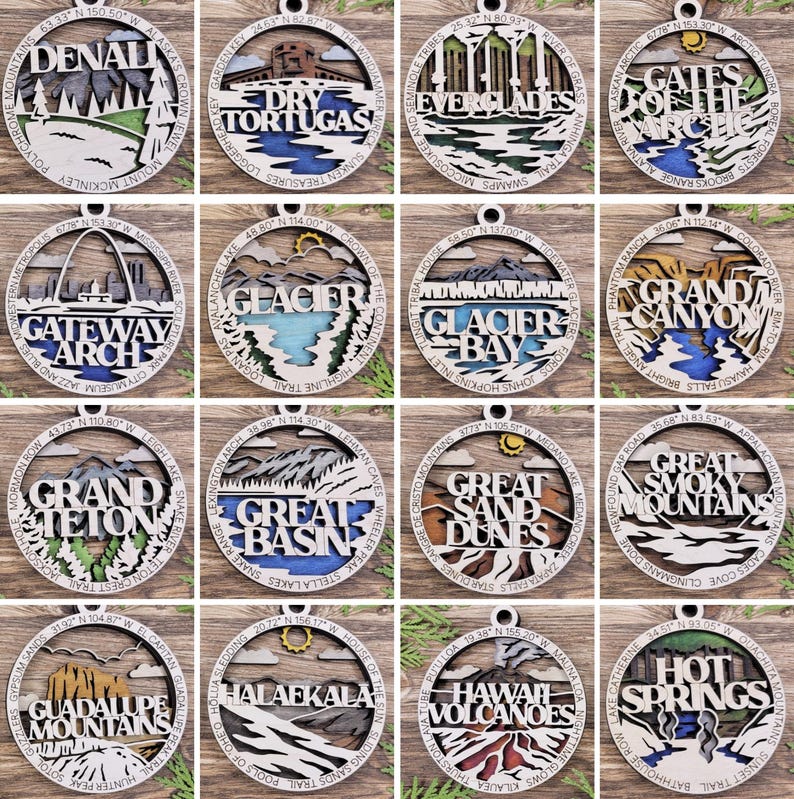 Puede incluir: Doce adornos de madera que representan diferentes parques nacionales de los Estados Unidos. Cada adorno es redondo y presenta una ilustraci&oacute;n detallada de un hito del parque, junto con el nombre del parque y sus coordenadas. Los adornos est&aacute;n pintados en varios tonos de marr&oacute;n, azul, verde y blanco.