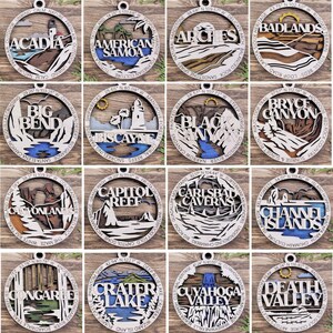 Puede incluir: Doce adornos de madera que representan diferentes parques nacionales de los Estados Unidos. Cada adorno es redondo y presenta un dise&ntilde;o detallado cortado con l&aacute;ser del paisaje del parque, incluyendo monta&ntilde;as, r&iacute;os y &aacute;rboles. El nombre del parque est&aacute; escrito en una fuente decorativa en cada adorno.