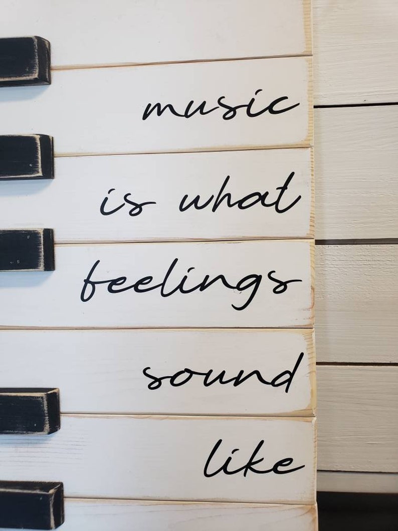 Puede incluir: Un letrero de madera blanco con detalles de teclas de piano negras. El letrero muestra la cita "la m&uacute;sica es lo que los sentimientos suenan" en escritura cursiva negra. Un art&iacute;culo decorativo.
