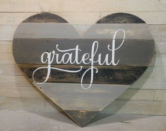 Puede incluir: Un letrero de madera en forma de corazón, de color gris y marrón, con la palabra "grateful" escrita en pintura blanca.