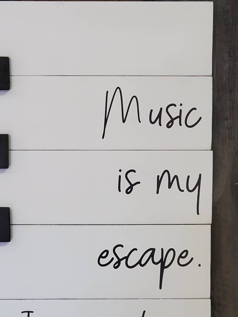 Puede incluir: Letrero de madera blanco con las palabras "Music is my escape" en letras cursivas negras. El letrero est&aacute; hecho de tablones de madera horizontales con acentos cuadrados negros. Una pieza decorativa para un amante de la m&uacute;sica.