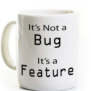 May include: White ceramic mug with a curved handle. The mug features the text "It's Not a Bug, It's a Feature" in black, bold font. The mug is designed for hot beverages.