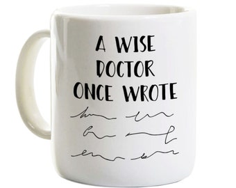 May include: White ceramic mug with black text that reads "A wise doctor once wrote" followed by a series of scribbled lines.