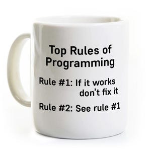 May include: White ceramic mug with the text "Top Rules of Programming." Rule #1: If it works, don't fix it. Rule #2: See rule #1. The mug has a curved handle and is suitable for hot or cold beverages.
