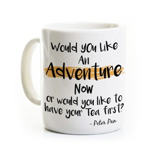 May include: White ceramic mug with a black and gold design. The mug features the text "Would you like an Adventure Now or would you like to have your Tea first?" with the quote "Peter Pan" at the bottom.