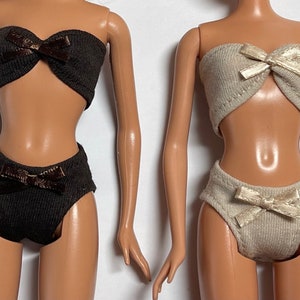 Könnte beinhalten: Zwei Puppen-Bikini-Sets, eines in Braun mit braunen Schleifen und eines in Beige mit beigen Schleifen.