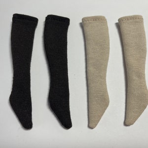 Könnte beinhalten: Vier Paar kniehohe Socken für Puppen. Zwei Paare sind schwarz und zwei Paare sind beige.