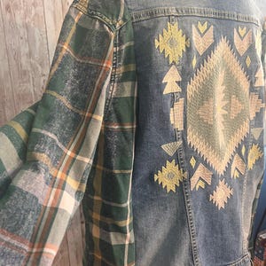 May include: Denim jacket with green plaid sleeves and embroidered geometric design on the back. The jacket features a button-down front and a collared neckline. The embroidery includes yellow and beige colors.