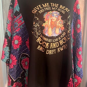 May include: Black t-shirt with a colorful floral design on the sleeves. The shirt features a graphic of a woman with sunglasses and the text "GIVE ME THE BEAT AND FREE MY SOUL, WANNA GET LOST IN YOUR ROCK AND ROLL AND DRIFT AWAY."