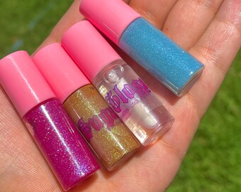 May include: Four small pink tubes of lip gloss with glitter. The tubes are labeled "Sugar Blast" with pink lettering. The glosses are in the colors pink, gold, clear, and blue.