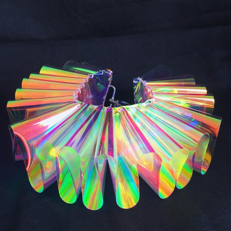 May include: A large iridescent collar made of multiple overlapping plastic panels. The collar is a circle and is made of a clear plastic that has a rainbow sheen.