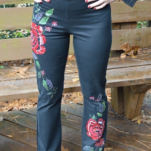 Puede incluir: Pantalones negros acampanados con bordado floral con rosas rojas y hojas verdes.