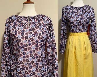 May include: A long-sleeved blouse with a floral print in shades of blue, purple, and red. The blouse has a gathered neckline and a loose fit.