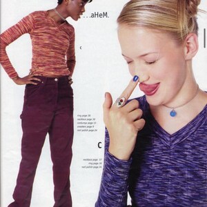 May include: A fashion magazine spread featuring two models. One model wears a long-sleeved, orange and brown striped shirt and burgundy pants. The other model wears a purple and gray long-sleeved shirt and a silver necklace with a blue pendant.
