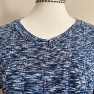 May include: A blue and white ribbed knit top with a V-neck. The fabric has a textured appearance. A beaded choker necklace with green and white beads is around the mannequin's neck.