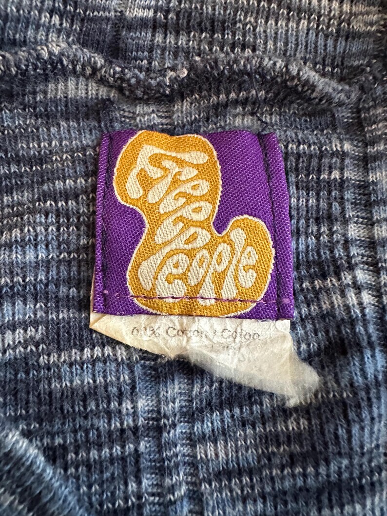May include: Close-up of a blue and white knit fabric with a purple tag. The tag features the words "Free People" in a gold, stylized font. A small piece of paper with text is attached to the tag.
