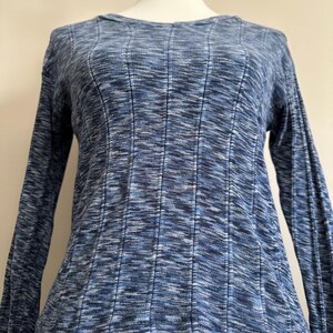 May include: A blue long-sleeve shirt with a ribbed texture. The shirt has a scoop neck and a fitted silhouette. The fabric has a subtle, mottled pattern in shades of blue and white.