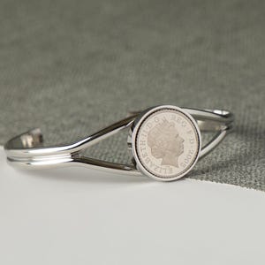 May include: A silver bracelet with a coin charm featuring a profile of Queen Elizabeth II. The coin is dated 2002.