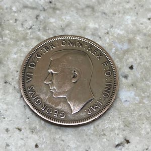 May include: A copper coin with the profile of King George VI and the inscription "GEORGIVS VI D:G:BR:OMN:REX F:D:IND:IMP:"