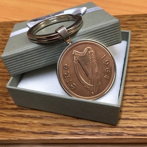 May include: A copper Irish coin keychain with a harp design and the year 1968. The coin is attached to a silver keyring.