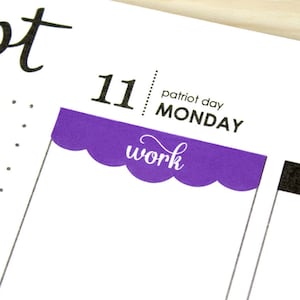 May include: A purple scalloped sticker with the word "work" written in white cursive. The sticker is placed on a calendar page for Monday, September 11th, with the text "patriot day" above it.