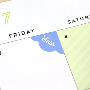 May include: A close-up of a calendar page with the word "Friday" and the number "3" written on it. A blue sticker with the word "class" is placed on the corner of the page, covering part of the number "4" on the next page.