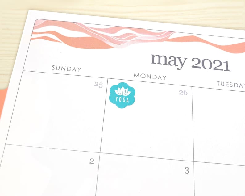 May include: A calendar page for May 2021 with a teal yoga sticker on the 25th. The sticker features a lotus flower and the word "YOGA". The top of the page has a peach and white wavy design.