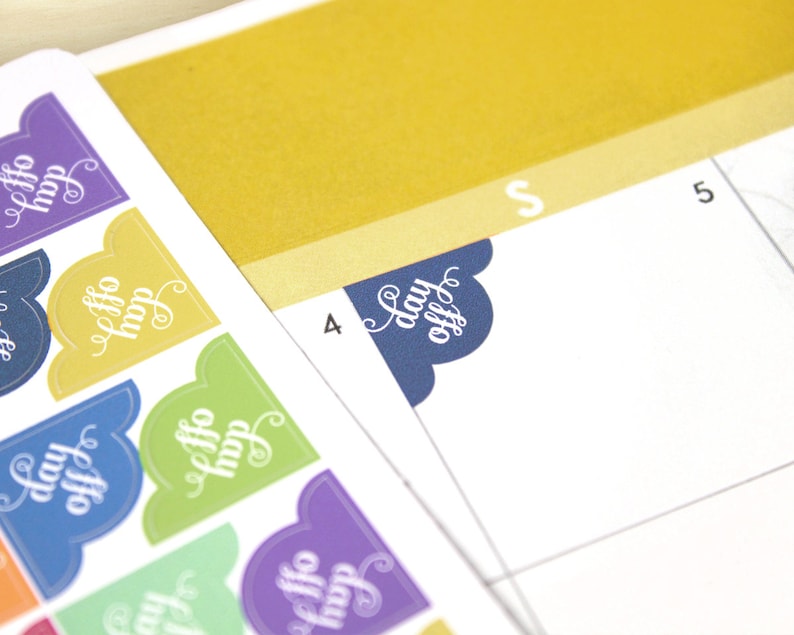 May include: Close-up of colorful planner stickers with the words "day off" in a decorative script. The stickers are in various colors, including blue, yellow, green, and purple. A calendar page is visible in the background.
