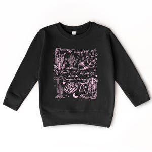 May include: Black sweatshirt with a pink graphic. The design includes cowboy boots, a horseshoe, a cactus, and the text "Boots and Bling, it's a Cowgirl thing." The design also features stars and a cowgirl hat.