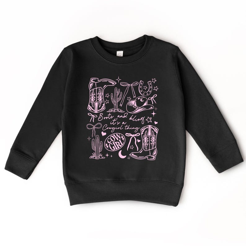May include: Black sweatshirt with a pink graphic. The design includes cowboy boots, a horseshoe, a cactus, and the text "Boots and Bling, it's a Cowgirl thing." The design also features stars and a cowgirl hat.