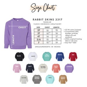 May include: A size chart for Rabbit Skins toddler fleece crewneck sweatshirts. The chart shows chest and length measurements in inches for sizes 2T to 7. Various sweatshirt colours are displayed, including black, white, pink, and navy.
