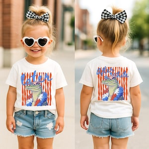 May include: A child's white t-shirt with a cartoon alligator wearing sunglasses and a feather boa. The front of the shirt says "Later" in blue script, and the back says "After a While". The alligator is in front of red and white stripes.
