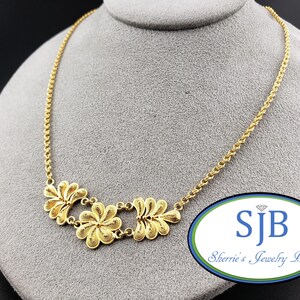 May include: A gold-toned necklace featuring a delicate chain and a central pendant composed of three interconnected floral-shaped filigree elements. The design showcases intricate wirework patterns within each petal, creating a textured appearance.