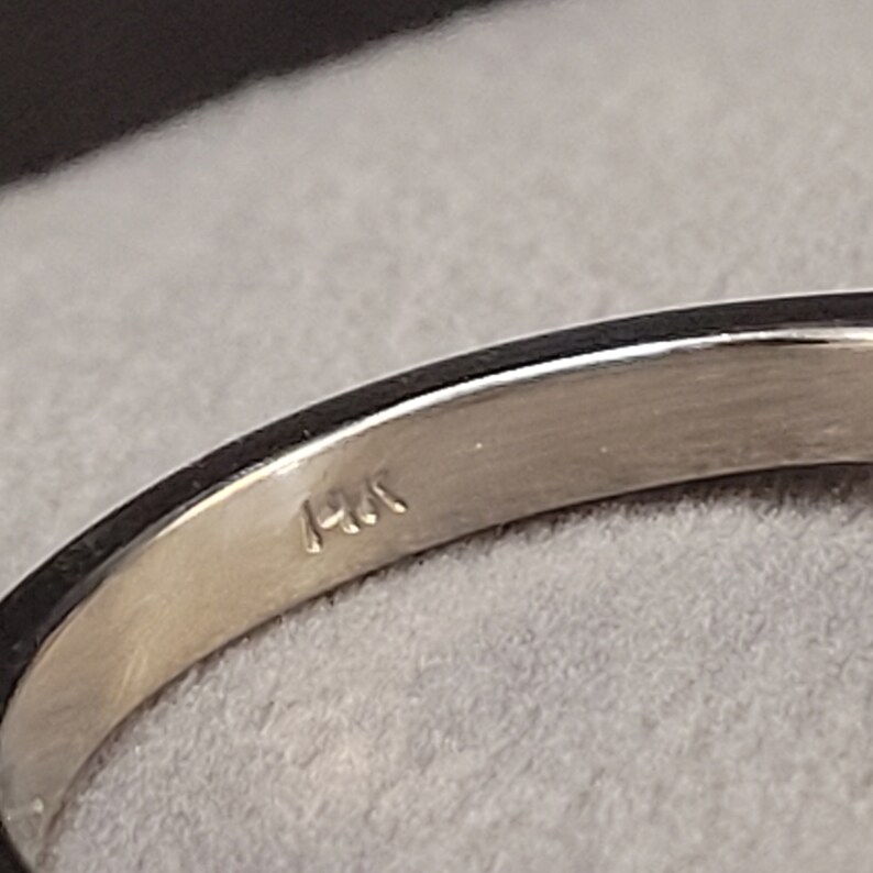 May include: Close-up of the inside of a silver ring with the inscription "14K" on the band.