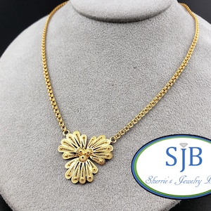 May include: A gold-toned necklace featuring a delicate filigree pendant shaped like a three-petaled flower. The pendant is attached to a fine chain link necklace. A logo with the text SJB and Sherrie's Jewelry Box is visible in the corner.