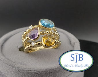 May include: A gold ring featuring three gemstones: a teardrop amethyst, a square citrine, and a round blue topaz. The ring is set with small diamonds on the band.