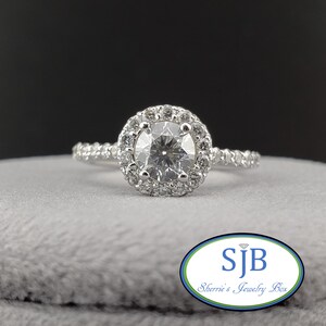 May include: A silver engagement ring with a round center diamond surrounded by a halo of smaller diamonds. The band is also set with smaller diamonds.
