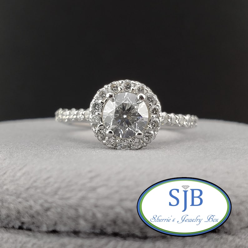May include: A silver engagement ring with a round center diamond surrounded by a halo of smaller diamonds. The band is also set with smaller diamonds.