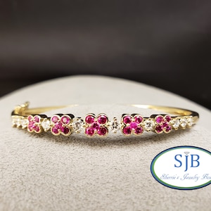Pode incluir: Uma pulseira de ouro com um design floral. A pulseira apresenta grupos alternados de pedras preciosas rosa brilhante e transparentes. As pedras preciosas são cravejadas em uma faixa de ouro. A pulseira é exibida em uma superfície cinza.