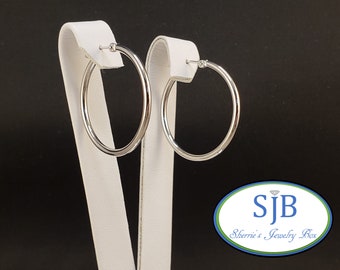 May include: A pair of silver hoop earrings on a white display stand. The earrings are simple and elegant, with a smooth, polished finish.