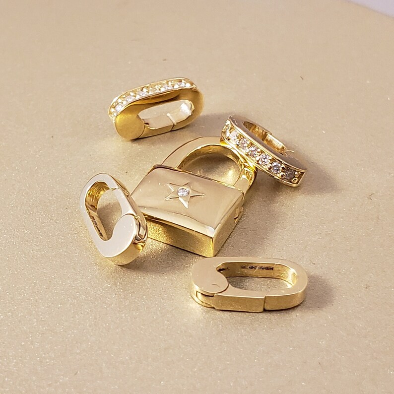 May include: Four gold-toned jewelry charms, including a padlock with a star-shaped diamond, a small oval charm, and two charms with rows of clear diamonds.