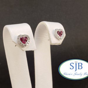 May include: A pair of heart-shaped earrings with a ruby center and a diamond halo. The earrings are on white display stands. The logo "SJB Sherrie's Jewelry Box" is visible in the lower right corner of the image.